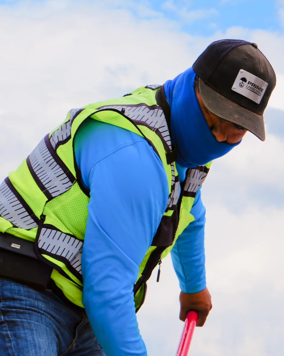 Prime Landscaping crew member in branded cap and hi-vis vest maintaining a property