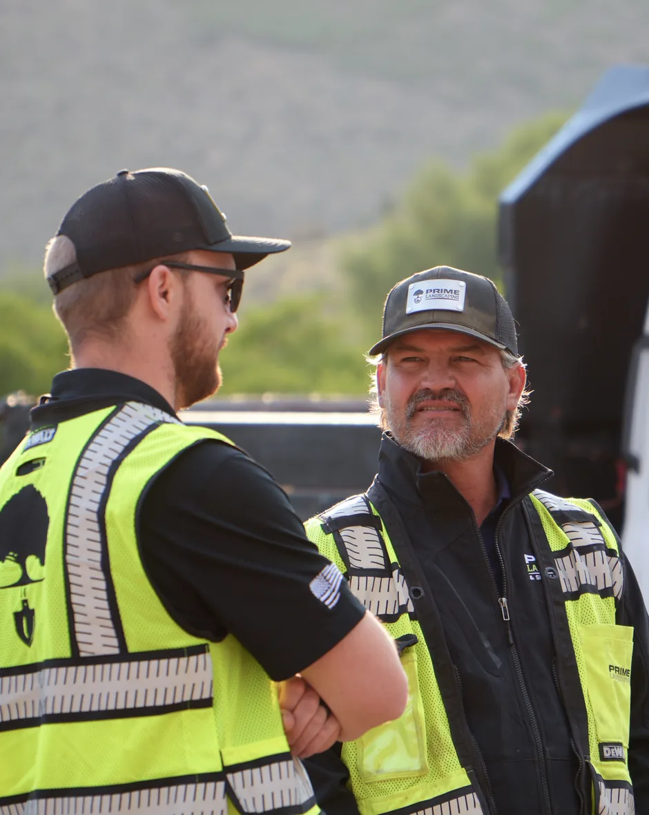 Prime Landscaping crew members in hi-vis vests talking on a job site